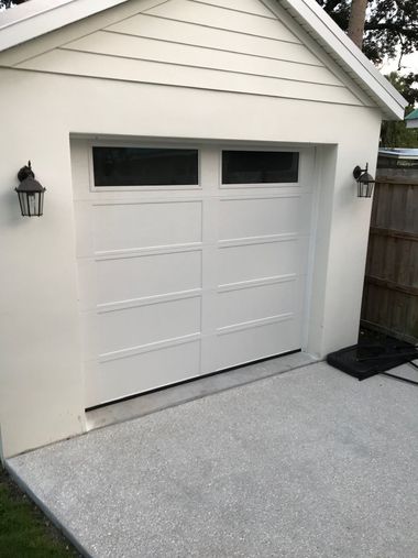 White double garage door with two small windows, beside a fenced driveway.