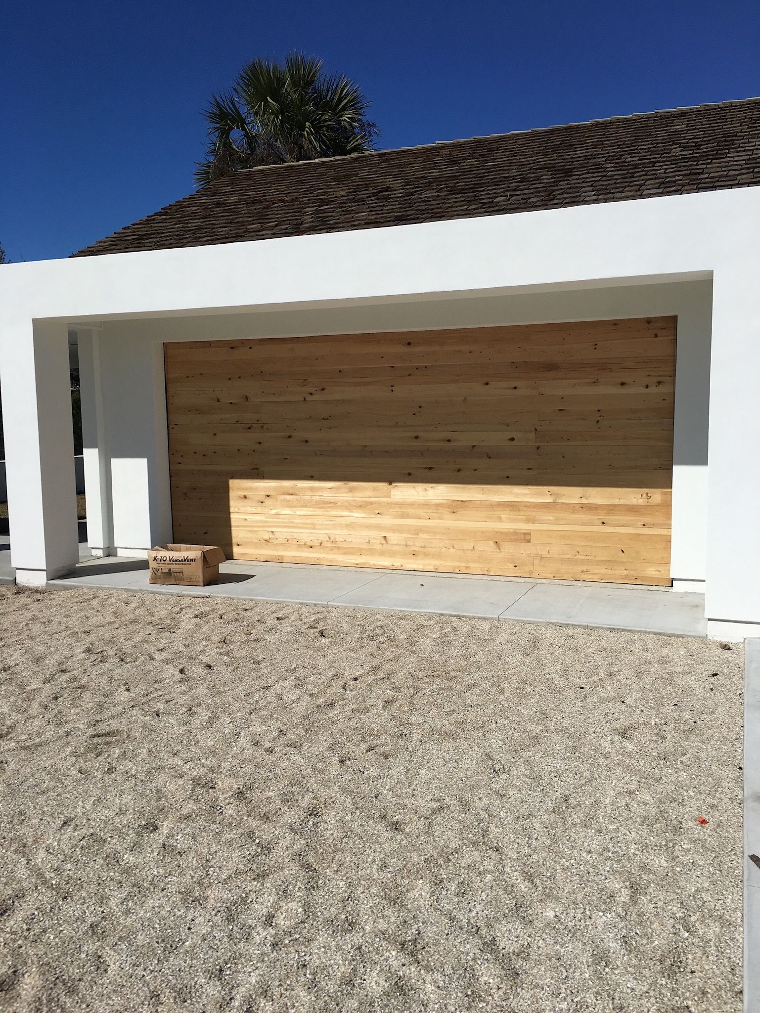 Modern white garage with wooden doors and stone driveway under a tiled roof