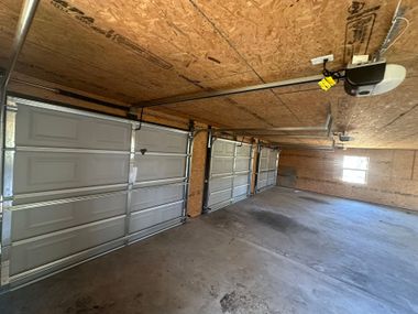 Empty garage interior with concrete floor, metal doors, and exposed plywood ceiling