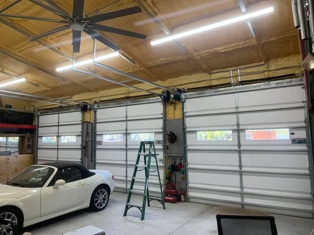Interior of a garage with a white convertible car, green ladder, and overhead garage doors under fluorescent lights