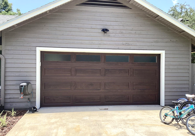 Two-car garage with dark brown door, gray siding, and bicycles on the right side.