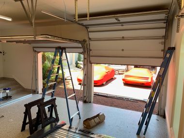 Garage interior with two ladders and a partly open door, revealing red cars outside.