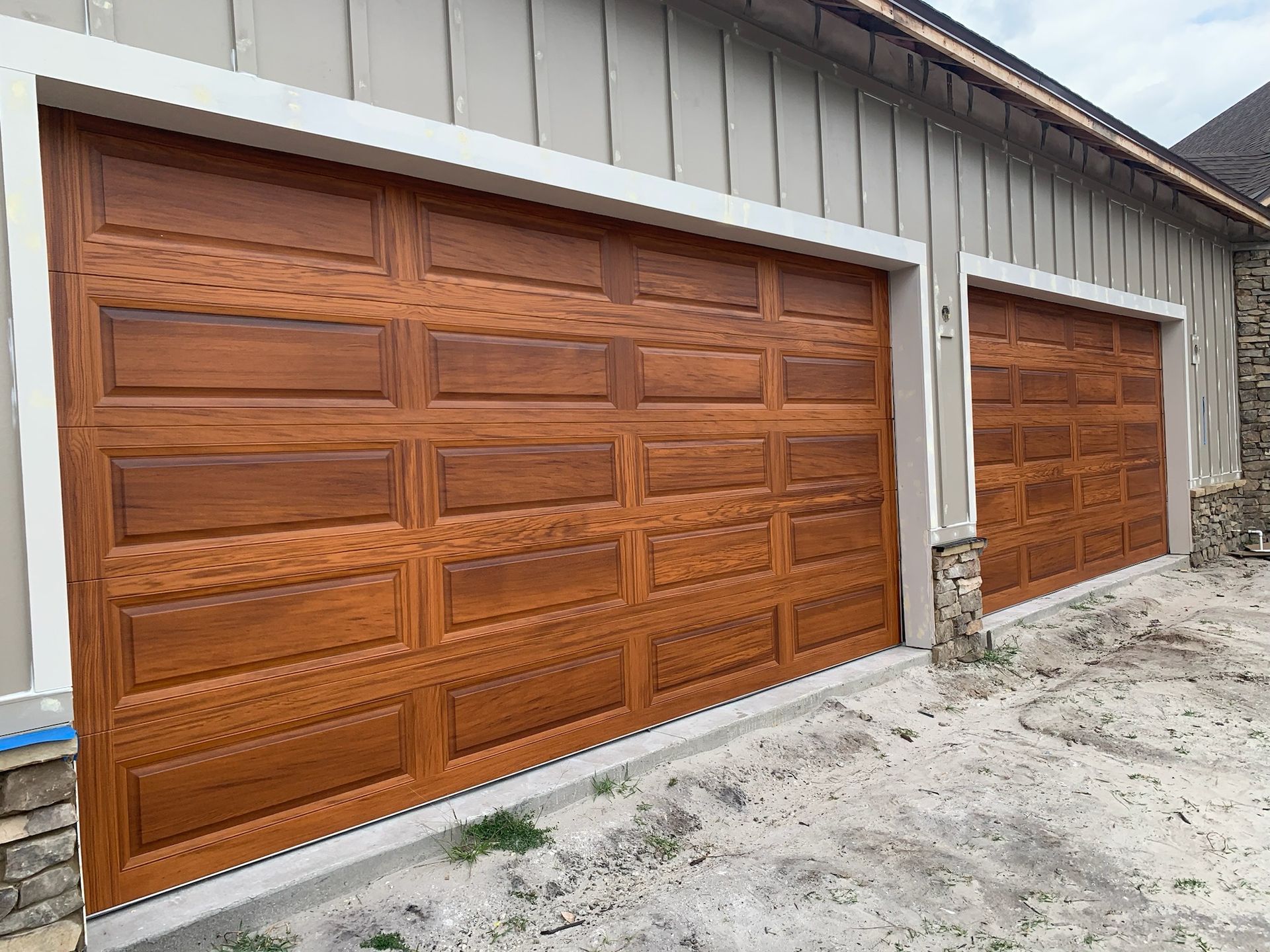 Wooden garage doors on a light gray building, viewed from an angle along a gravel driveway.