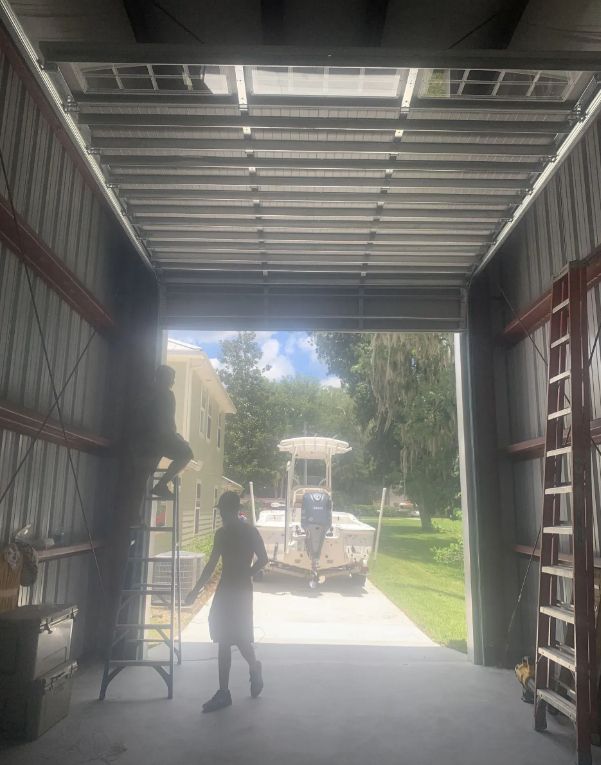 Inside a metal garage, a person stands near the open doorway, looking out at a golf cart on a grassy drive.