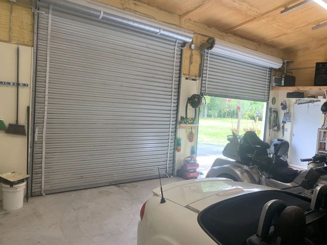 Garage interior with two metal roll-up doors, a motorcycle, and a car under repair.