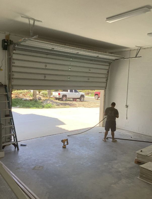 Person spraying or cleaning the floor inside an open garage with the door raised halfway open.