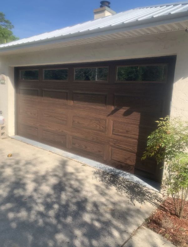 Brown wooden garage door on a stucco house, with driveway and sunlit shadows.