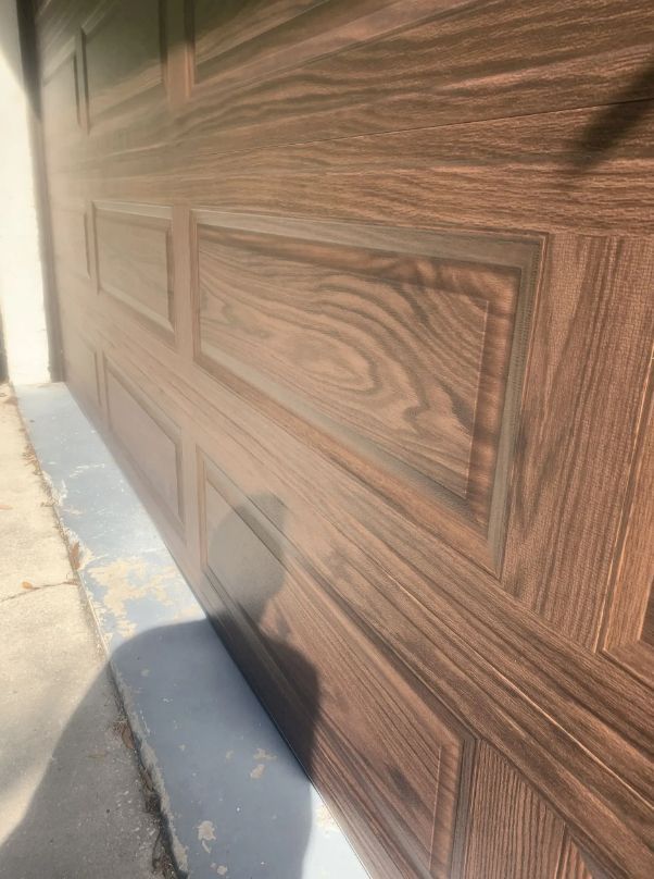 Close-up of a brown wood-grain garage door beside a sidewalk and curb in sunlight