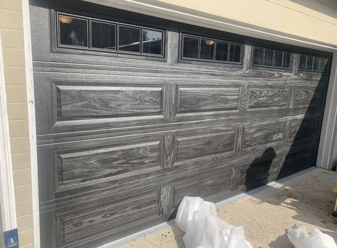 Partially open black garage door covered in protective plastic at a house entrance