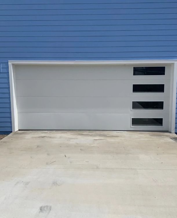 White modern garage door with four dark windows against a blue exterior wall.