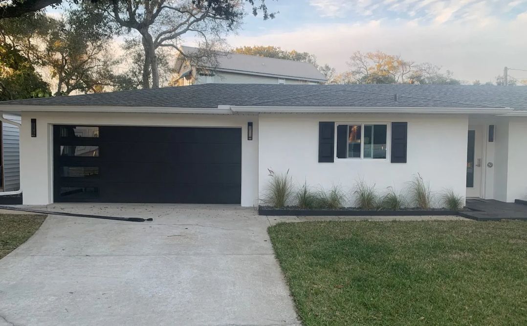 Single-story white house with a dark garage door, front lawn, and concrete driveway at dusk