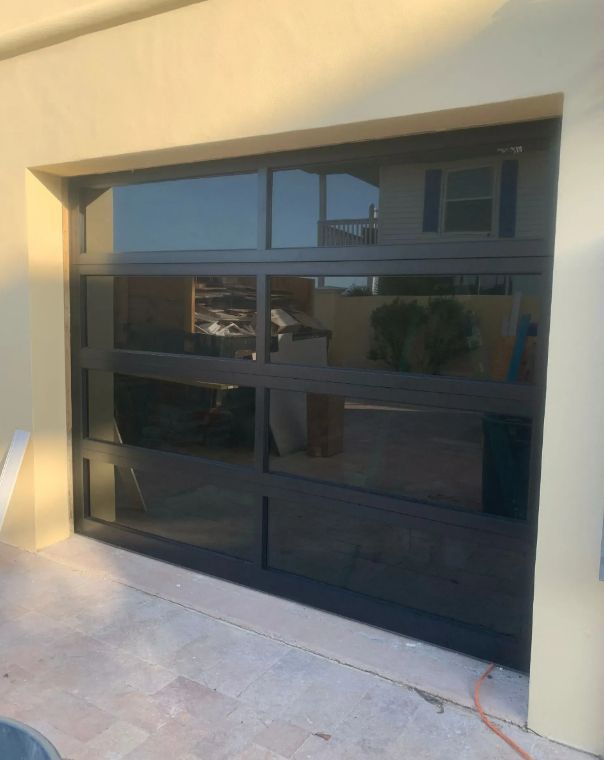 Black glass garage door set in a beige exterior wall, reflecting the driveway and nearby houses.