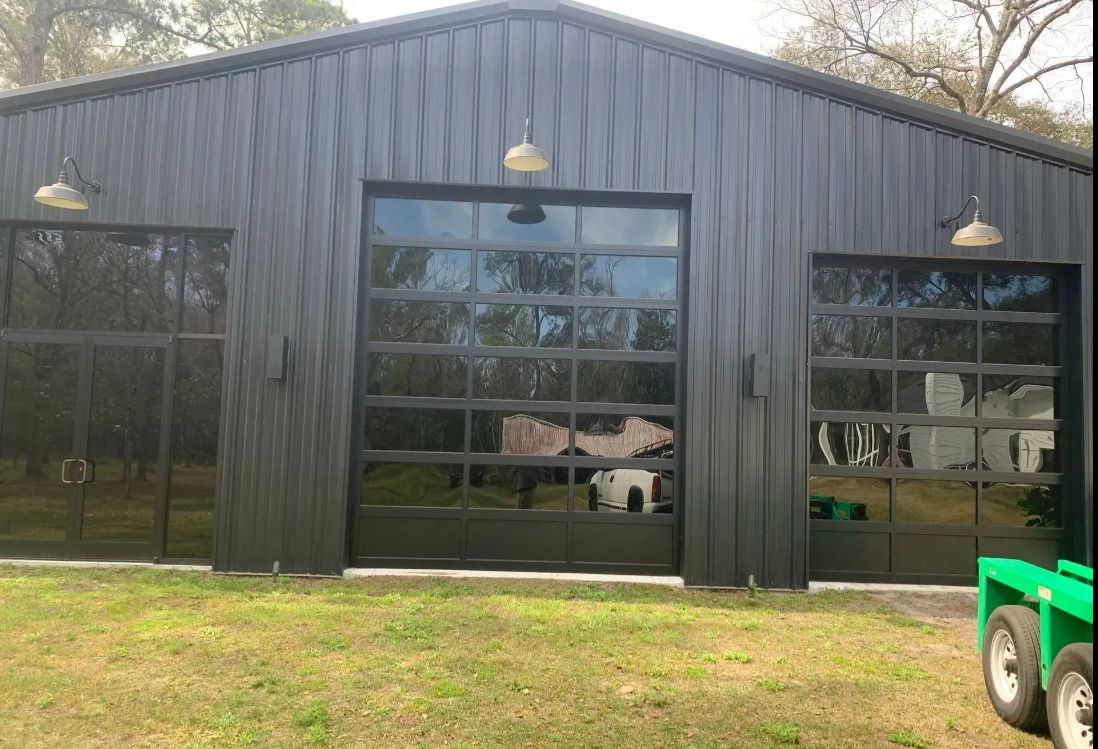 Black metal building with large glass windows and doors, reflected trees, and a green vehicle at right