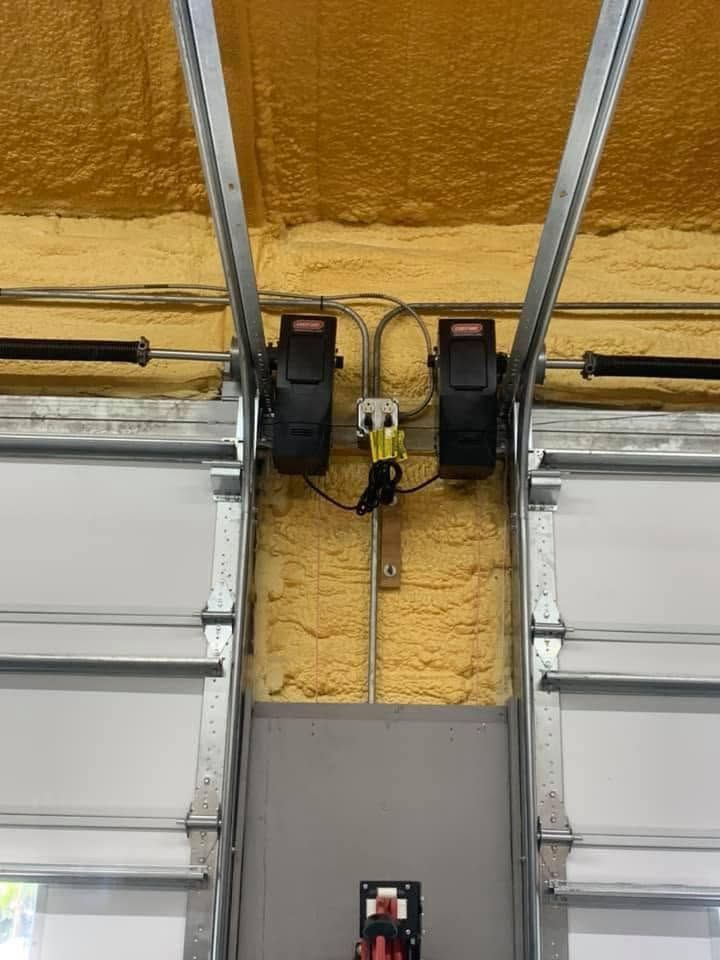 Garage door opener motors mounted above a partially open garage door with yellow insulation.