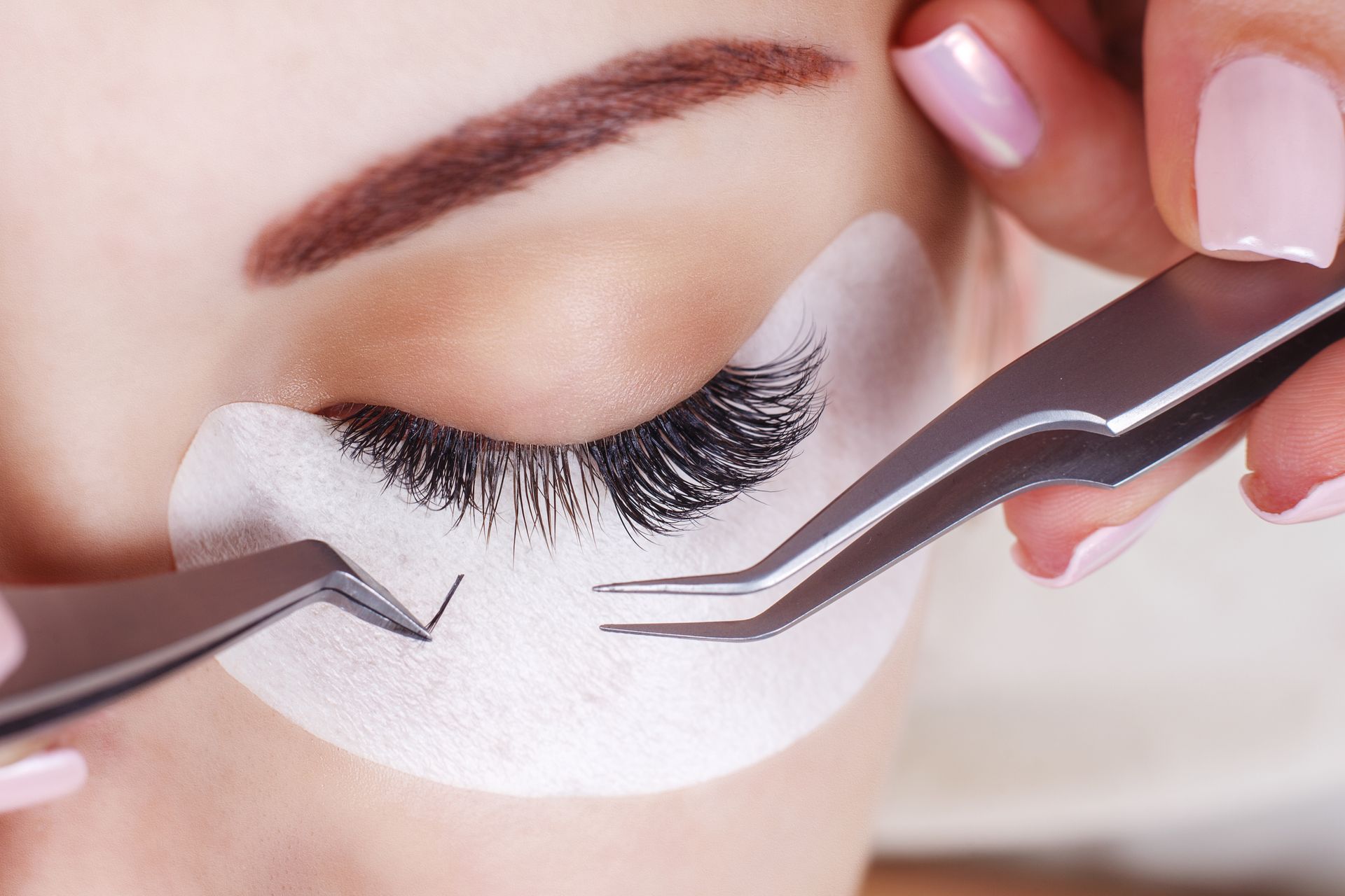 A woman is getting her eyelashes done with tweezers.