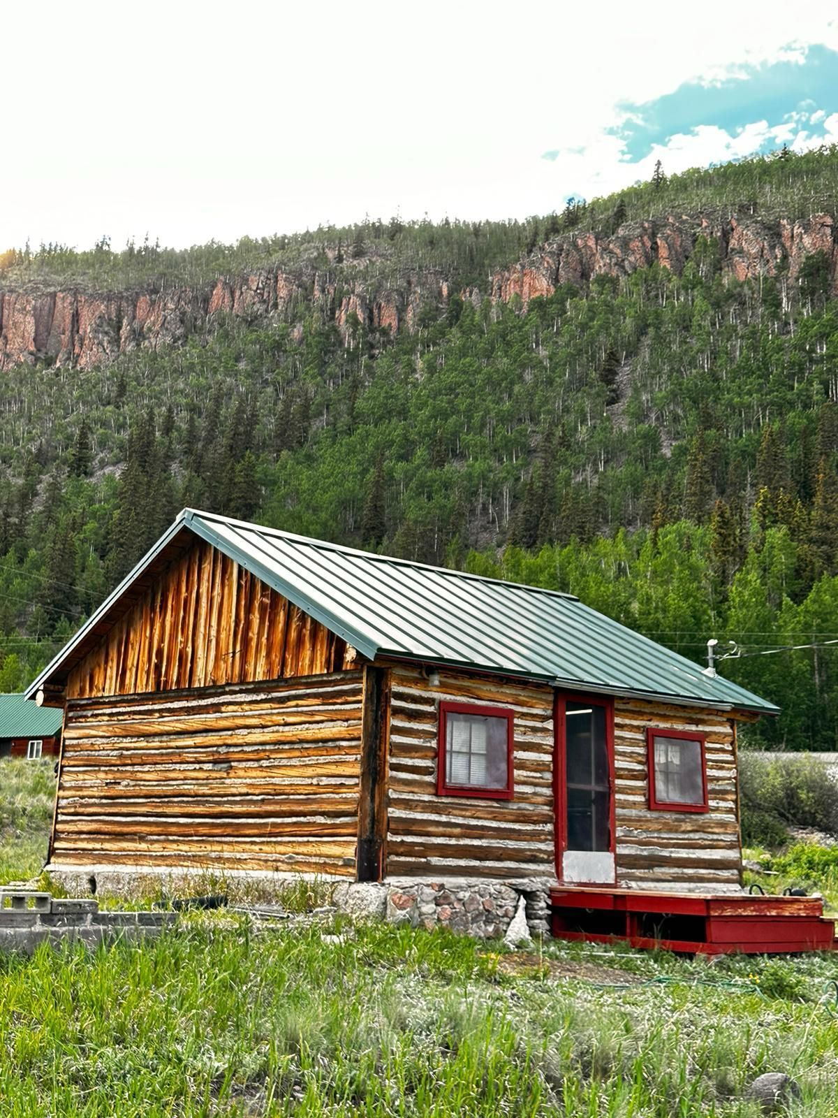 A log cabin with a green roof sits in the middle of a grassy field