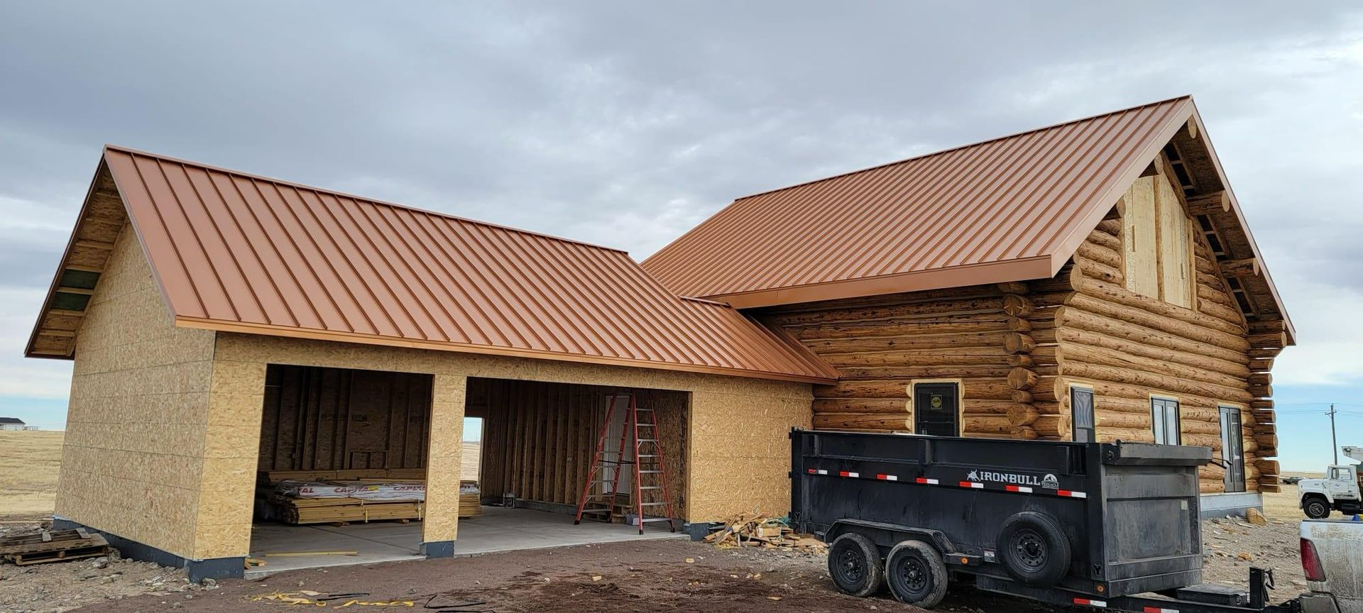 A black dumpster is parked in front of a house under construction