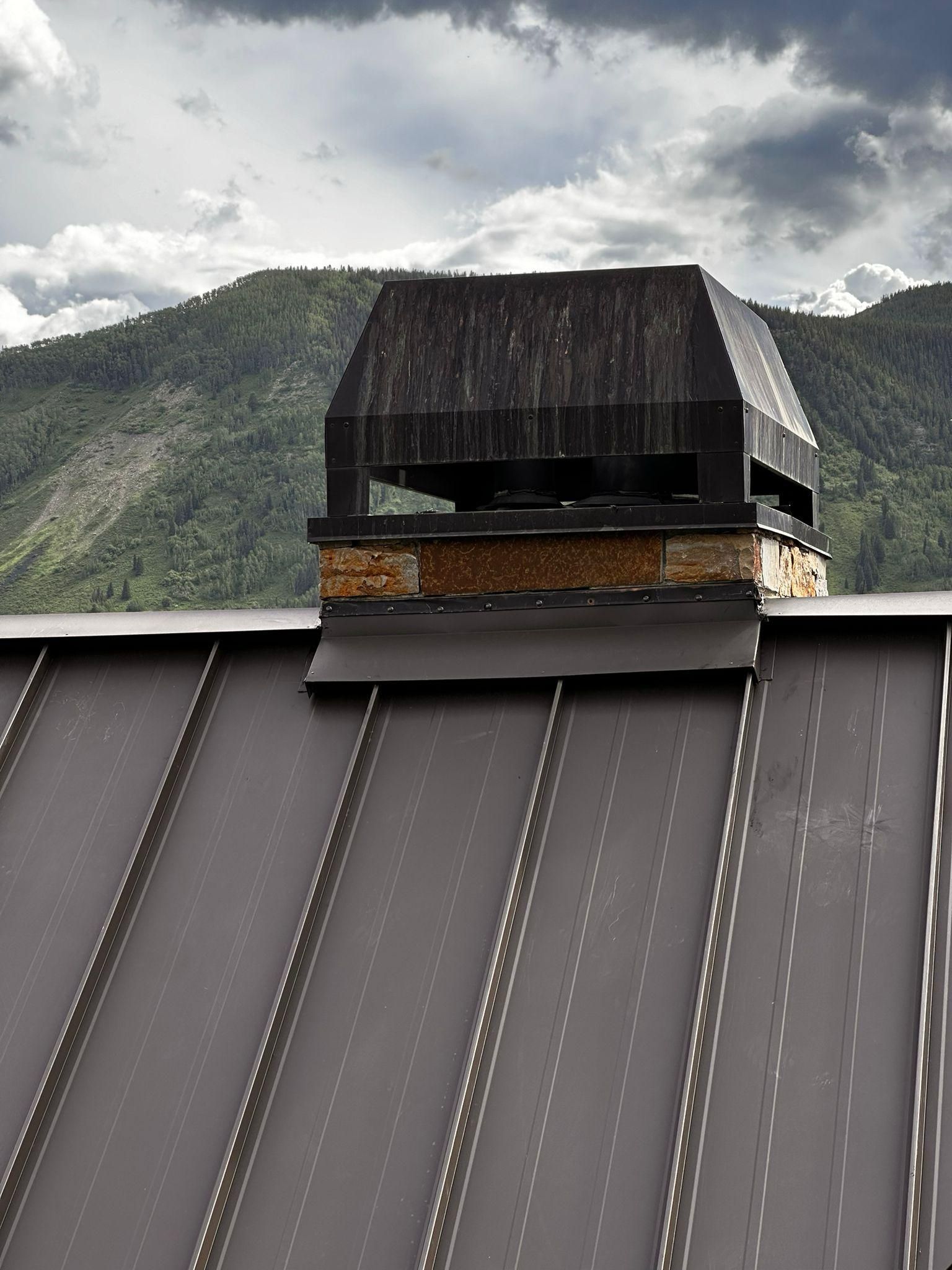 A chimney on top of a roof with mountains in the background