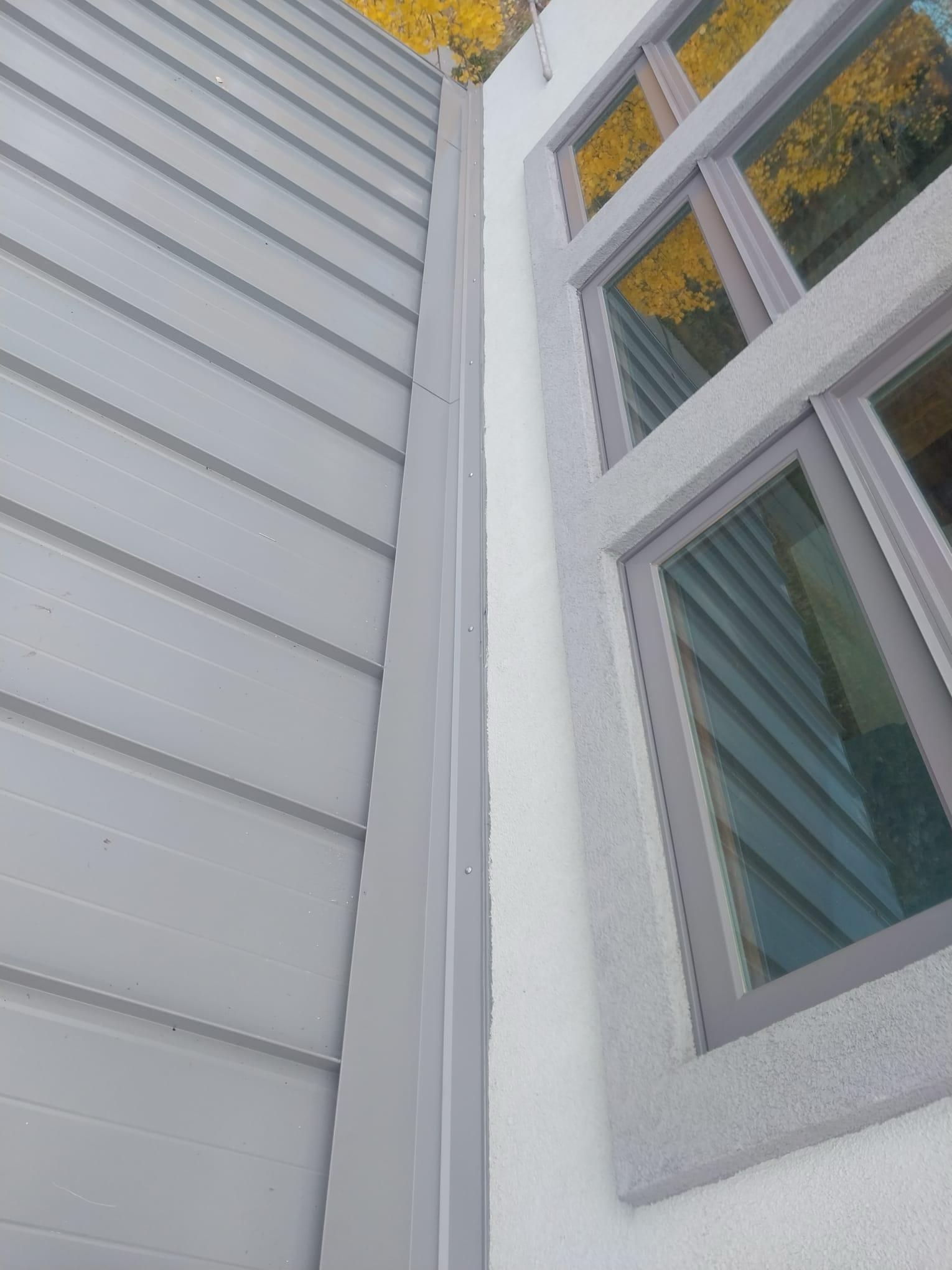 A corner of a building with a gray siding and two windows
