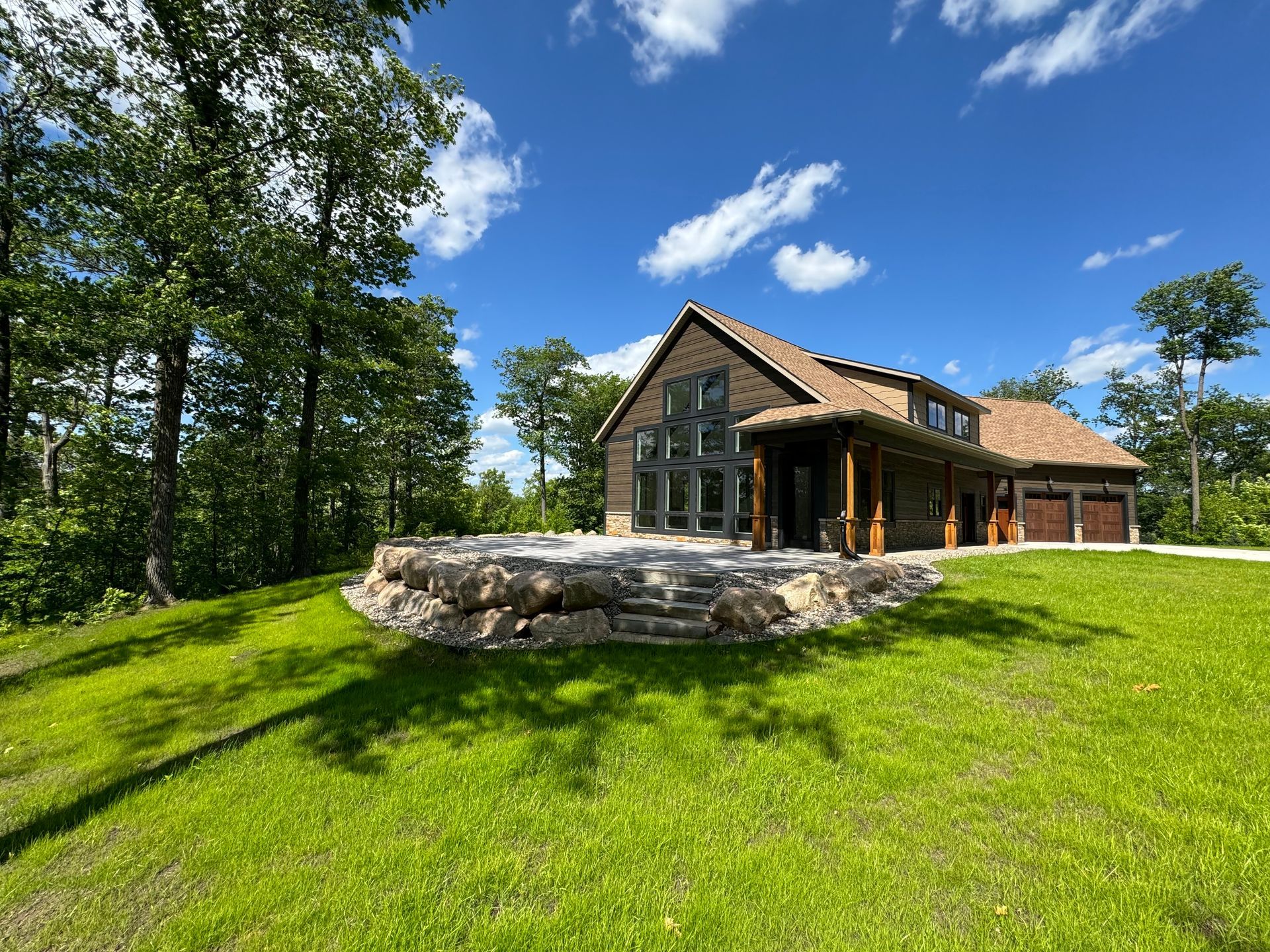 Modern house with stone patio, green lawn, trees, and blue sky.