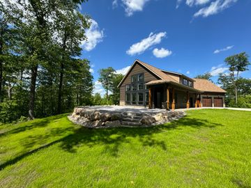Modern house with stone patio, green lawn, trees, and blue sky.