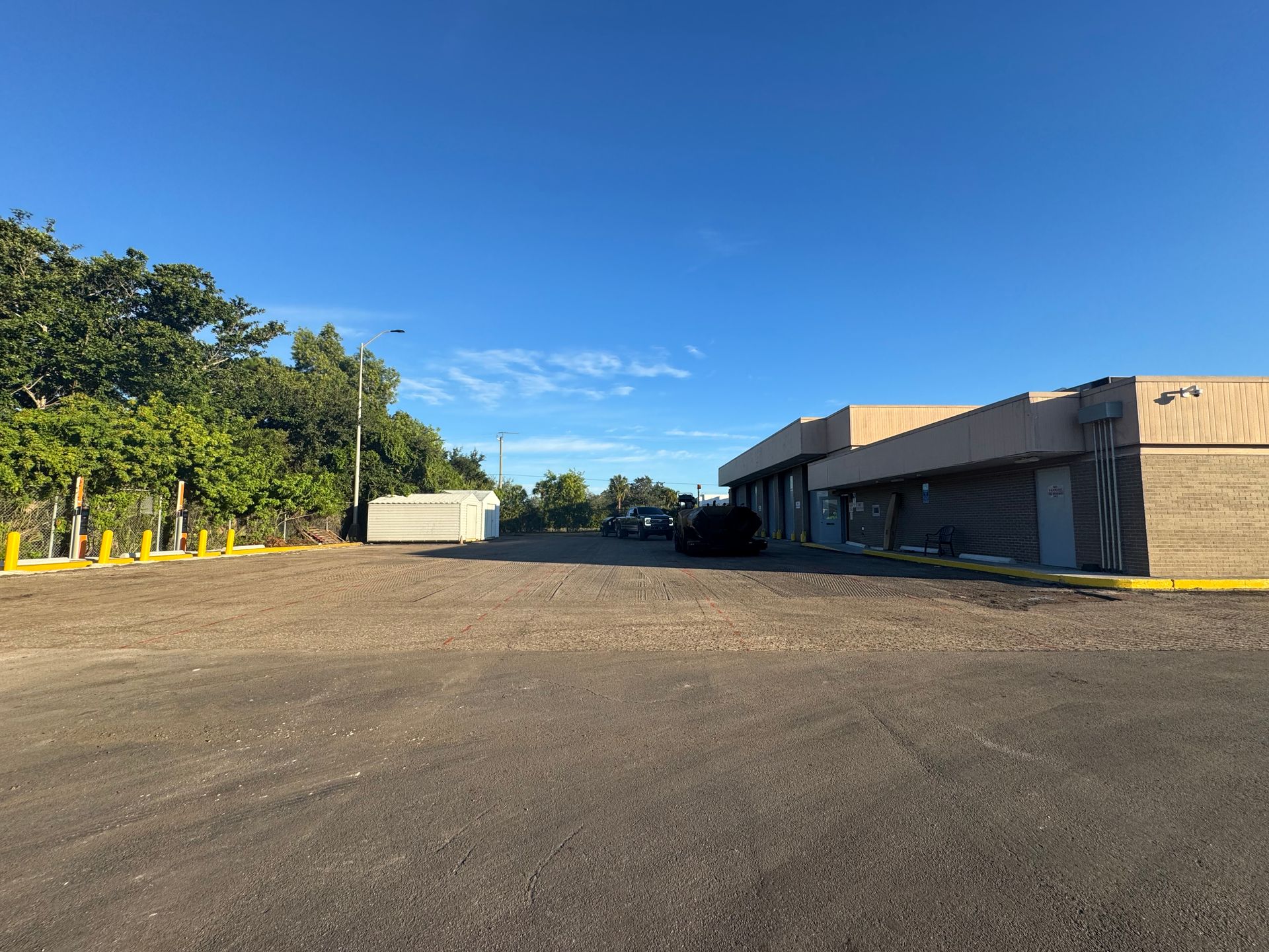 A large empty parking lot with a building on the right, trees and blue sky.