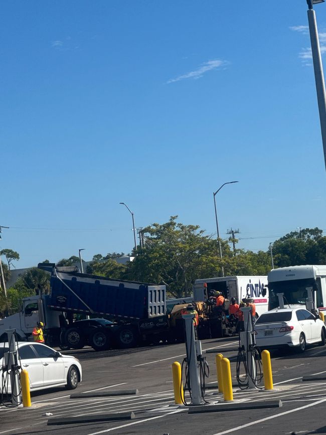 Road resurfacing; dump truck unloading asphalt, workers, cars. Blue sky, sunny day.