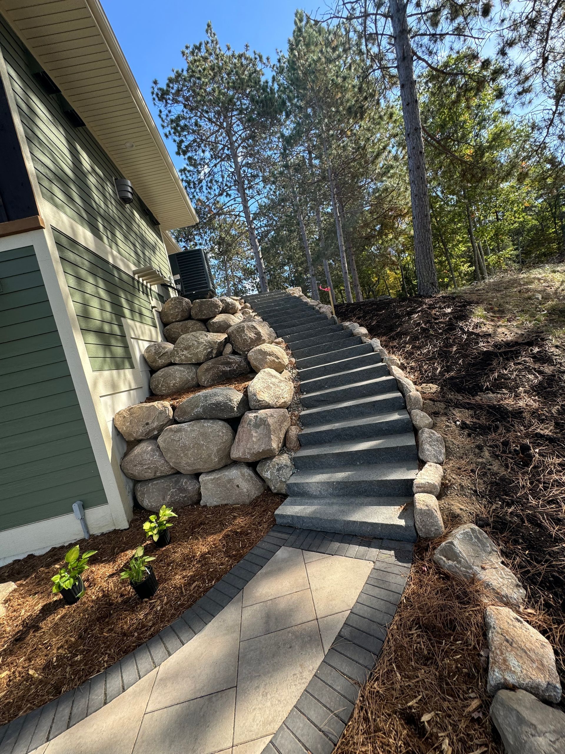 Stone steps and walkway leading uphill past a retaining wall, adjacent to a green-sided building.
