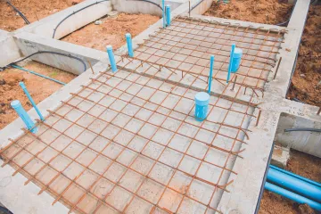 Construction site with exposed rebar, blue pipes, and concrete foundation.