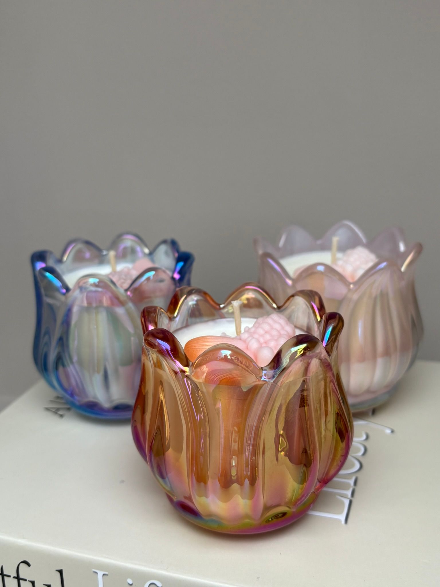 Drie decoratieve glazen kaarsenhouders in iriserend blauw, roze en amber op een witte achtergrond.