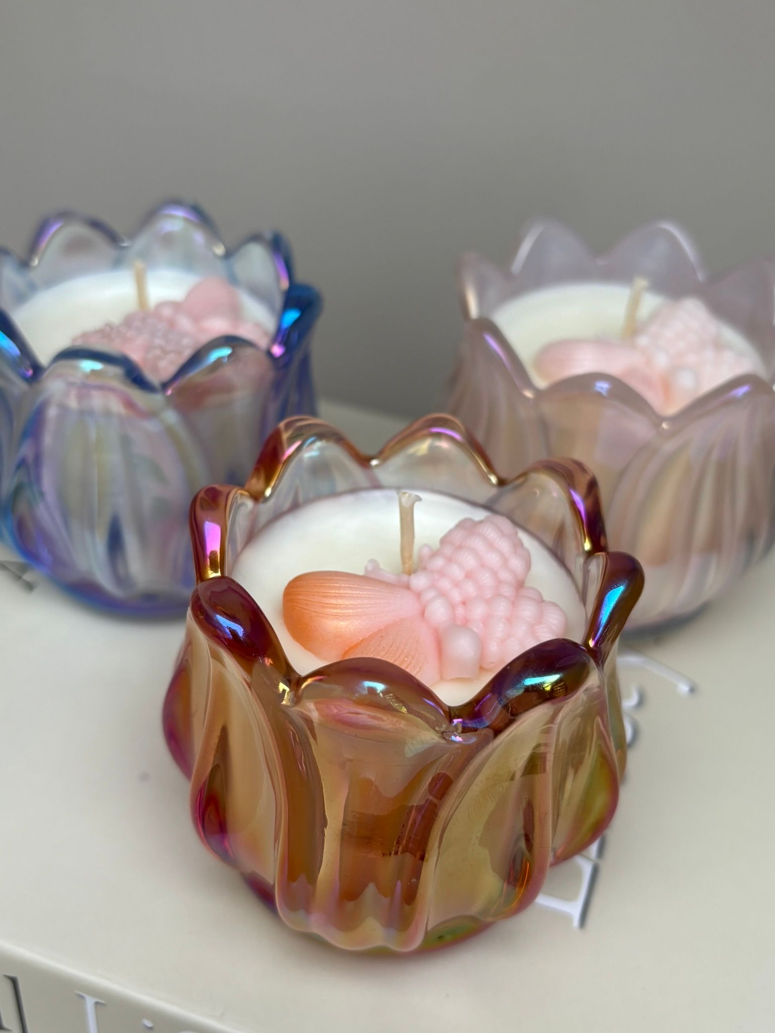 Drie decoratieve glazen kaarsenhouders in iriserend blauw, roze en amber op een witte achtergrond.