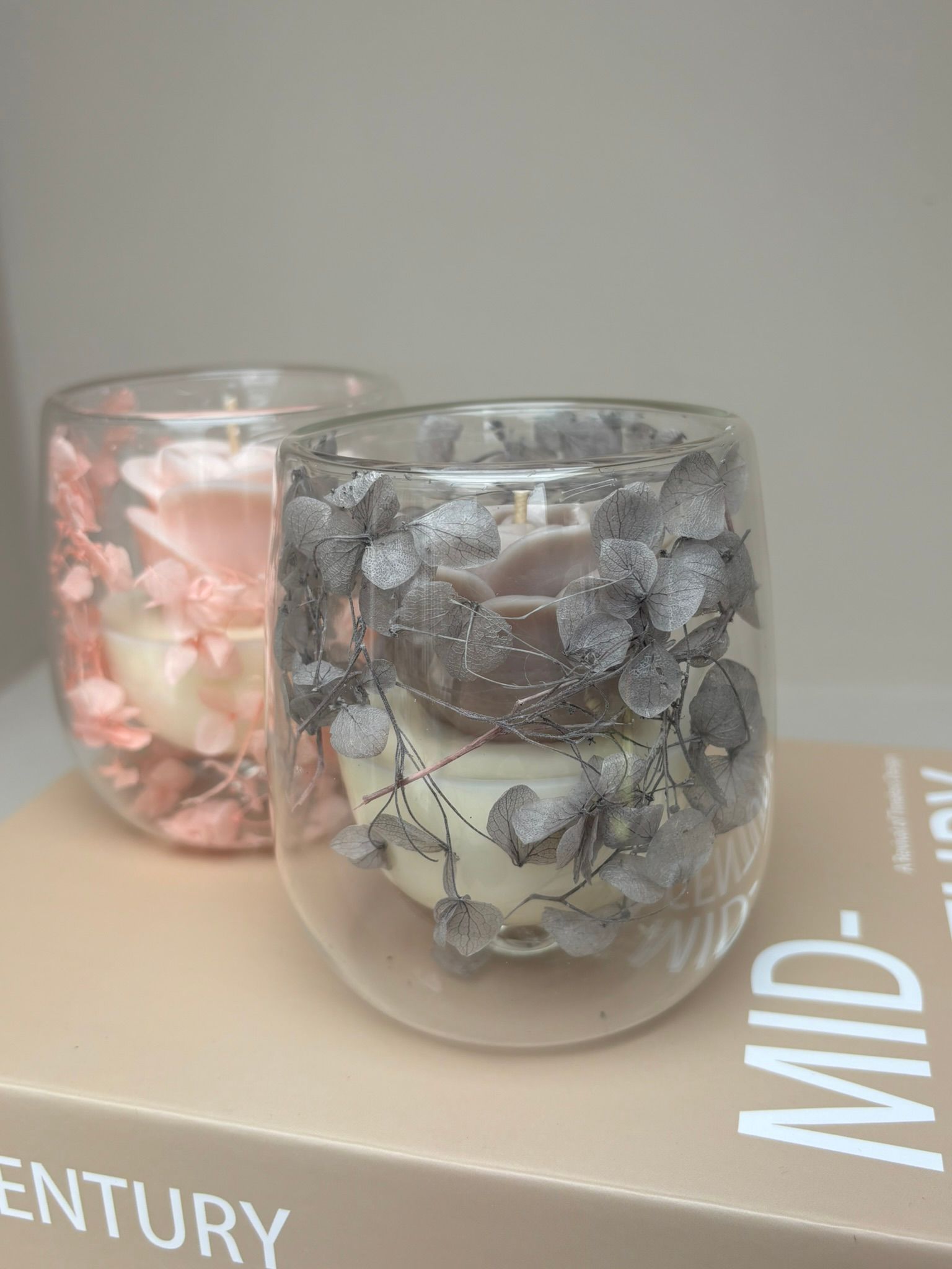 Twee kaarsen van mat glas met bloemmotieven op een beige boek of doos.