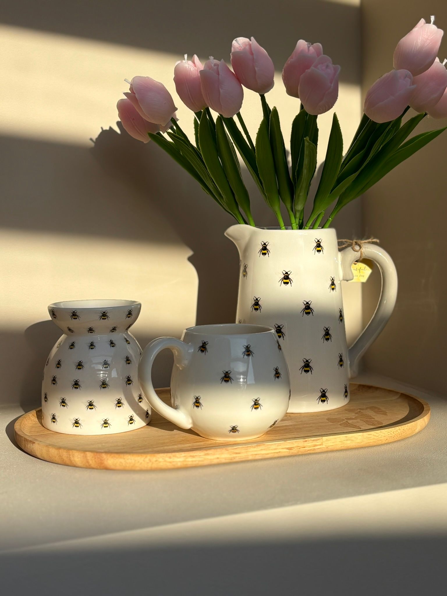Witte keramische kan met bijenmotief op een houten dienblad in het warme zonlicht.
