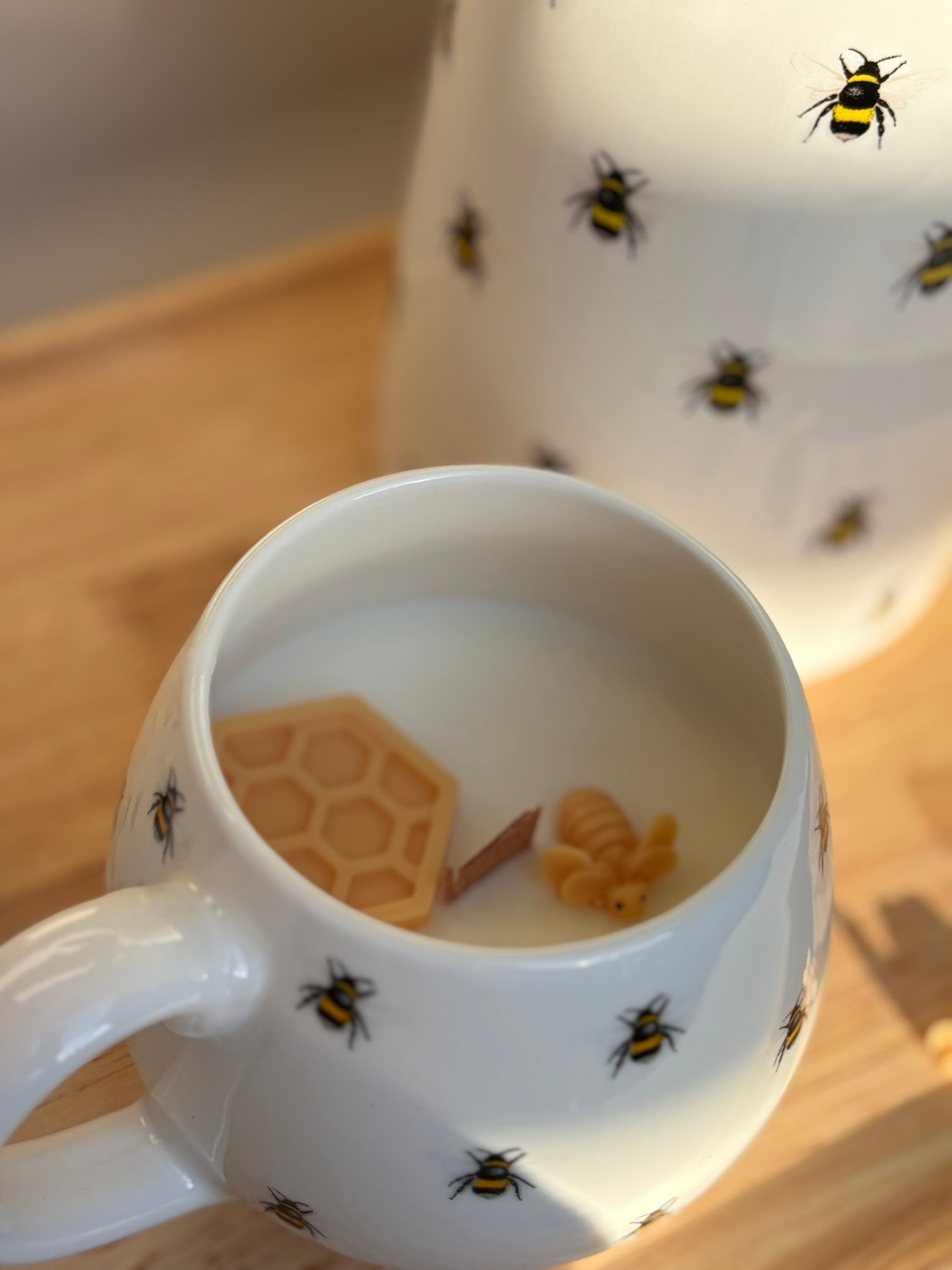 Witte mok en kan met bijenmotief, met honingraatvormige koekjes in de mok op een houten tafel.
