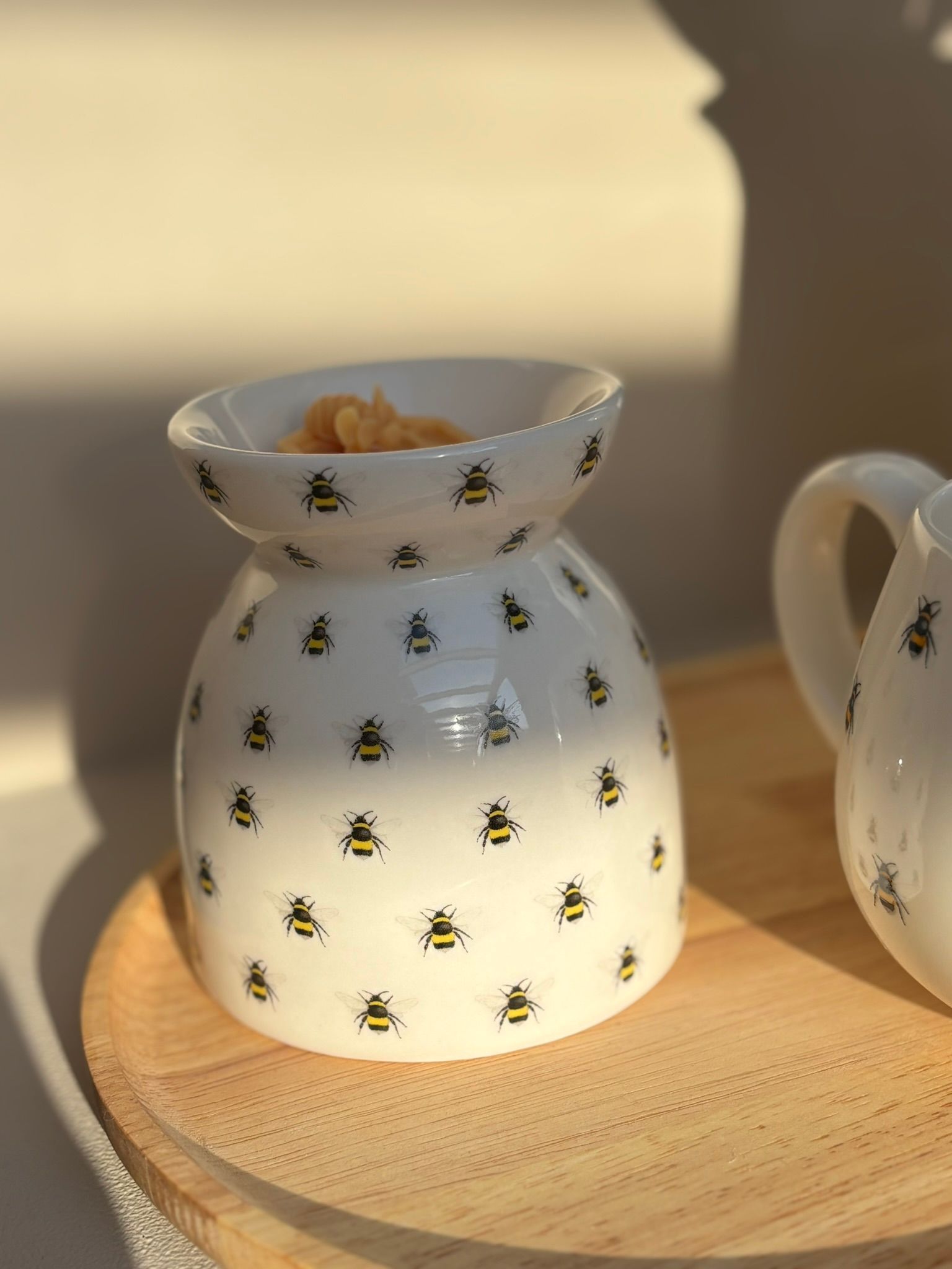 Witte keramische kan met bijenmotief op een houten dienblad in het warme zonlicht.
