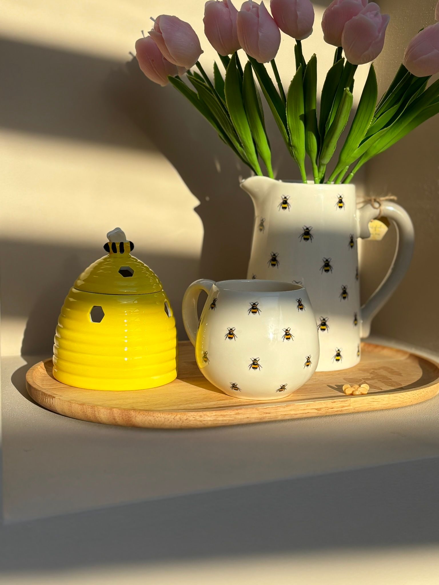 Een gele bijenkorfvaas en een witte vaas met sterrenpatroon, gevuld met tulpen, staan ​​op een plank in de zon.
