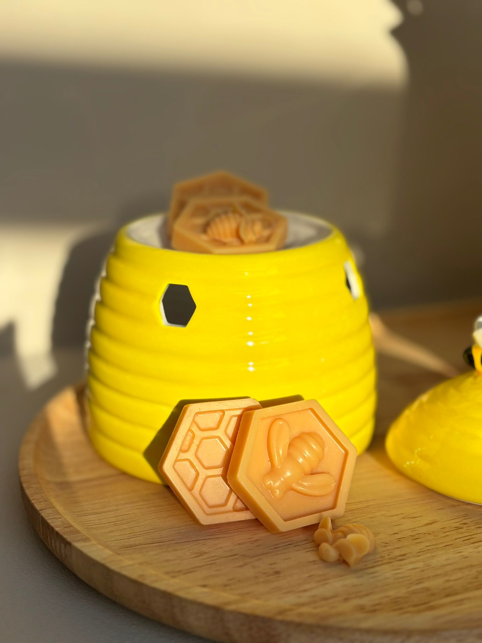 Gele bijenkorfvormige container op een houten dienblad met honingraatvormige zeshoekige koekjes en een klein bijtje als detail.