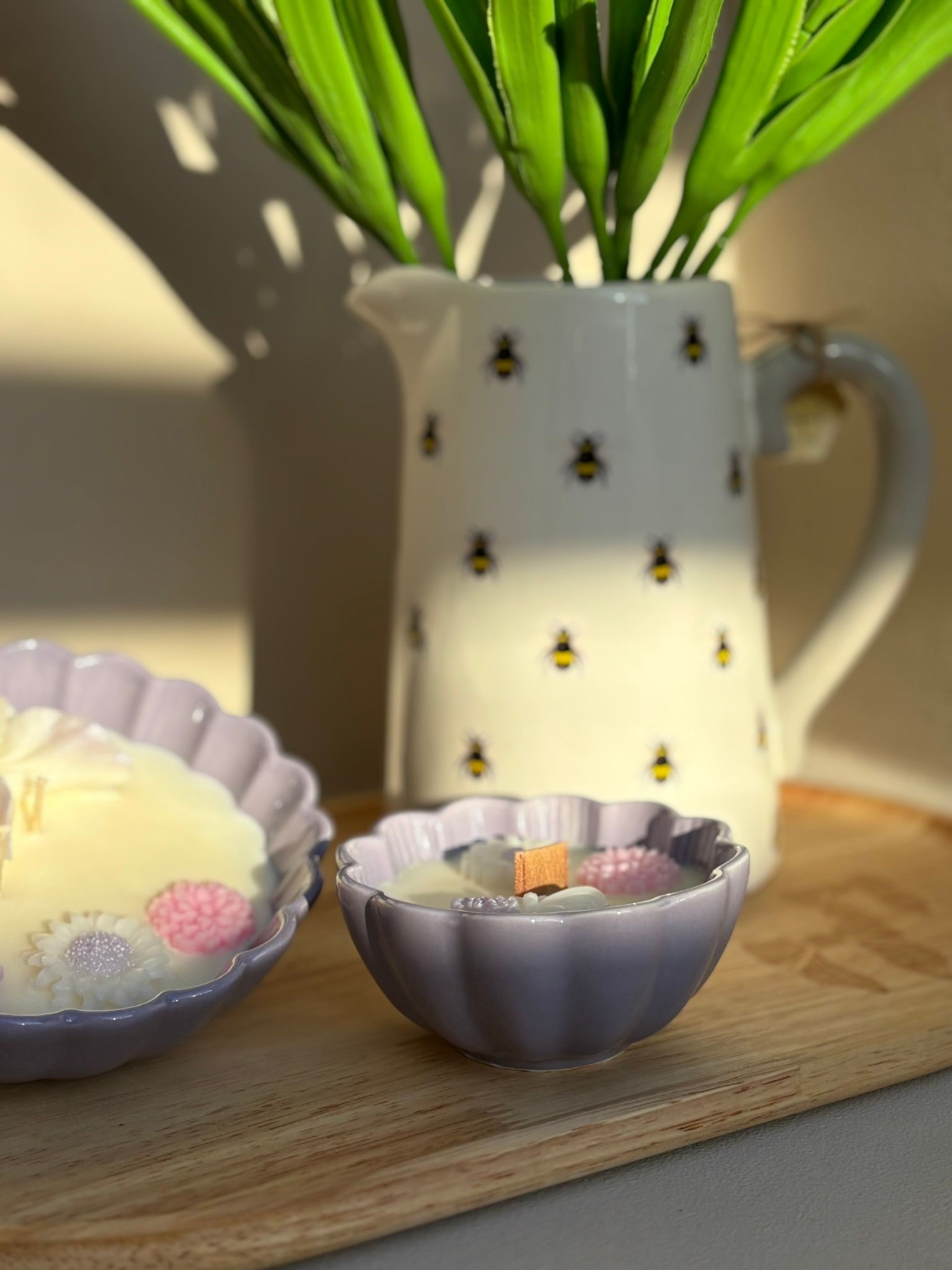 Een pastelkleurig, bloemvormig schaaltje met een lichtgroene kaars erop, op een tafel voor een bakje met bijenmotief.
