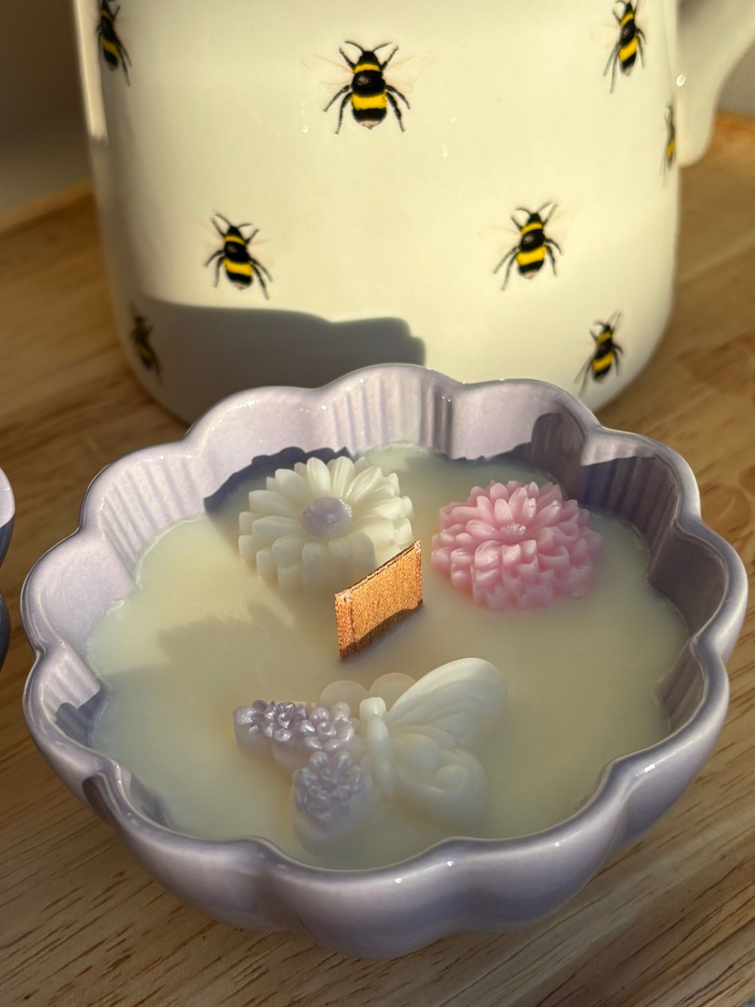 Een pastelkleurig, bloemvormig schaaltje met een lichtgroene kaars erop, op een tafel voor een bakje met bijenmotief.