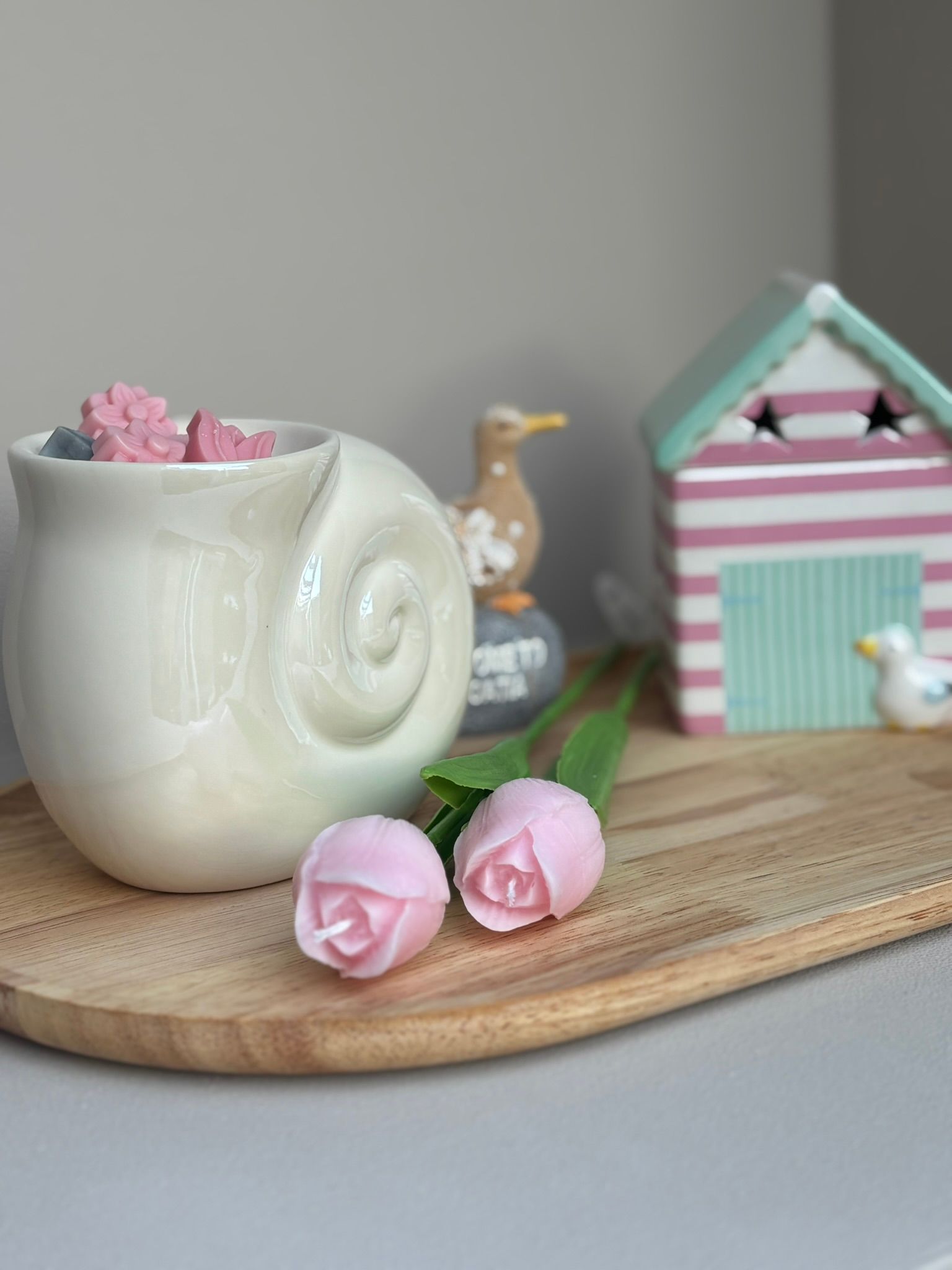 Witte, slakvormige keramische vaas met roze bloemen en twee roze rozenknopjes op een houten dienblad.