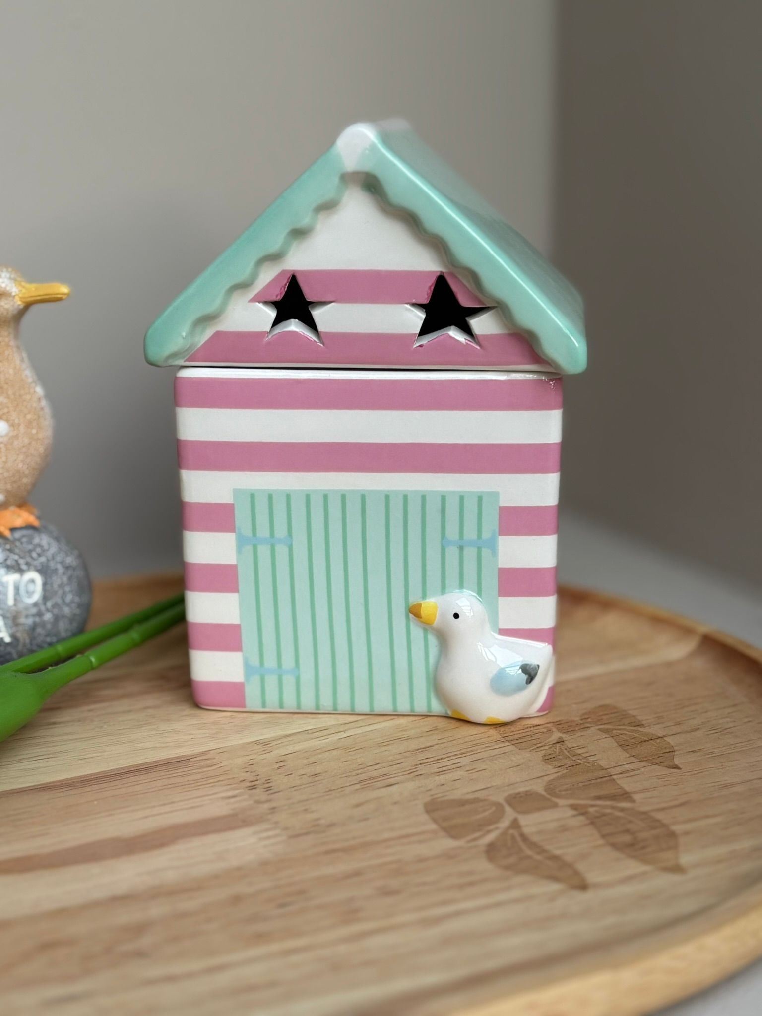 Roze gestreept miniatuurhuisje met mintgroen dak en deur, zwarte stervormige ramen, op een houten ondergrond met een klein vogeltje.