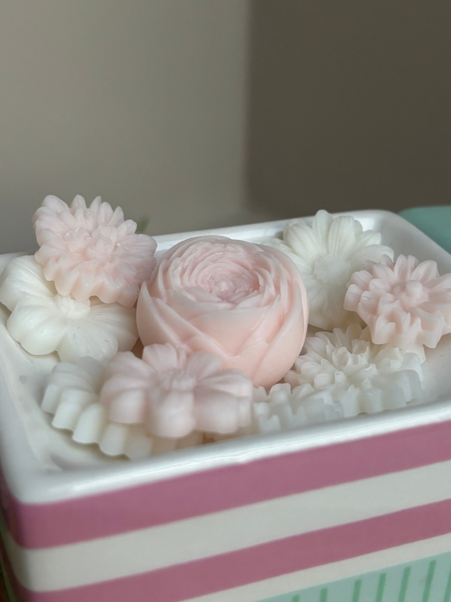 Roze en witte bloemvormige kaarsen in een gestreepte roze-witte houder.