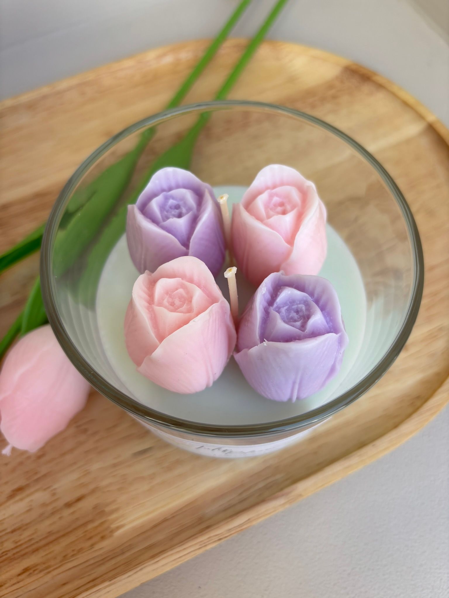 Vier pastelroze en lavendelkleurige roosvormige snoepjes in een glazen schaal op een houten dienblad.
