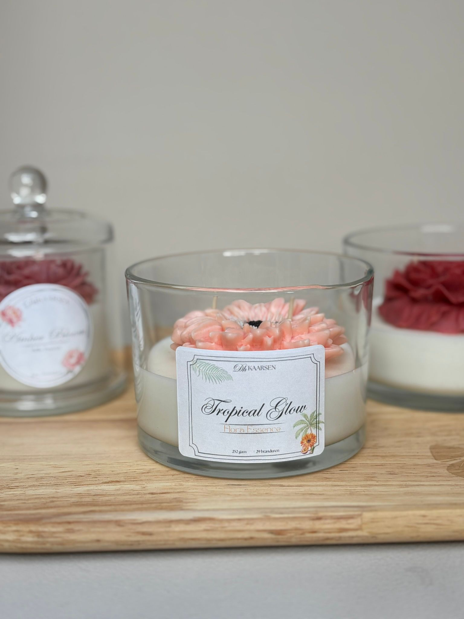 Drie decoratieve kaarsen in glazen potjes op een houten dienblad, met roze, rode en witte was.