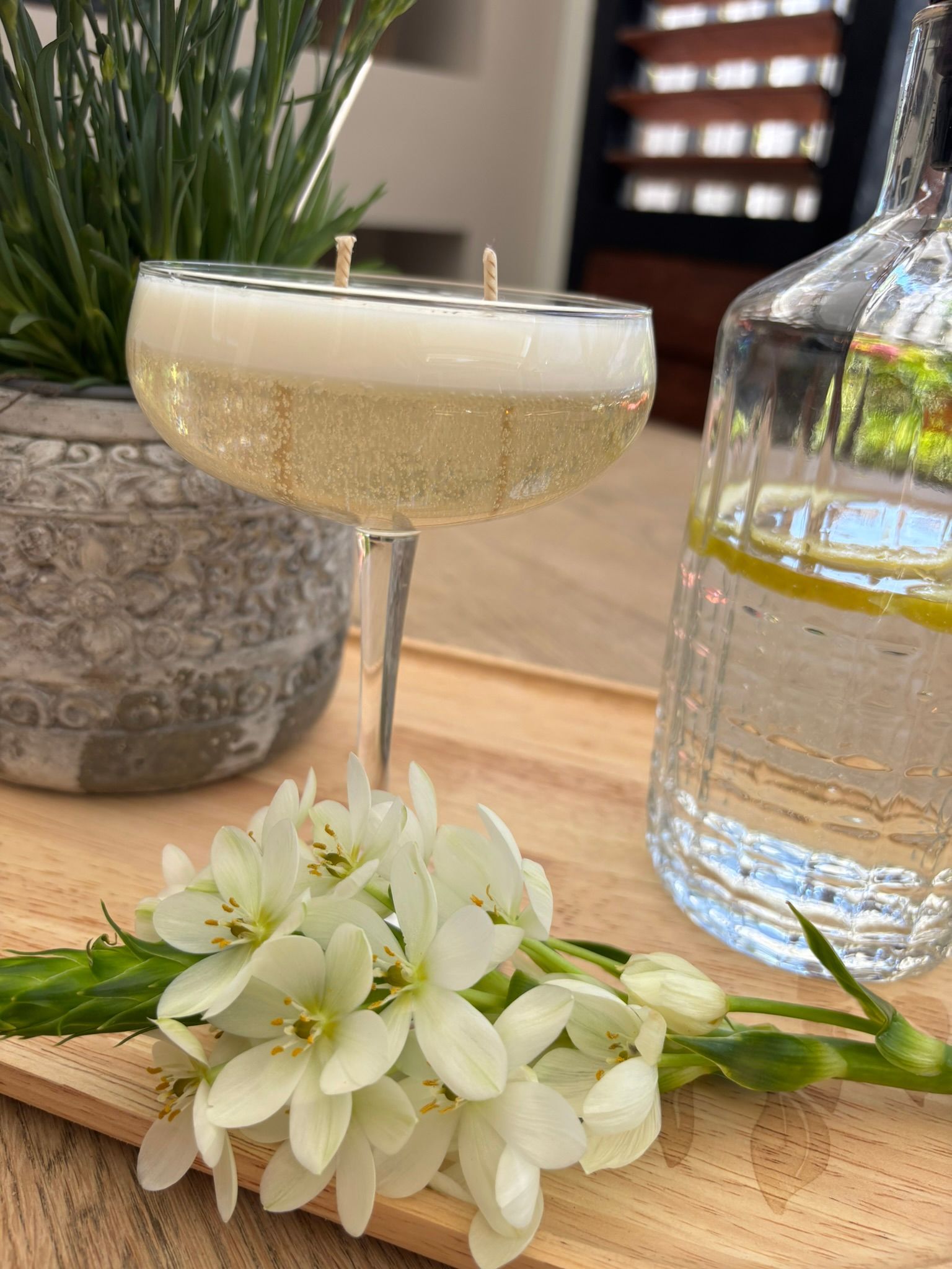 Champagneglas op een tafel met witte bloemen en een glazen karaf op de achtergrond.