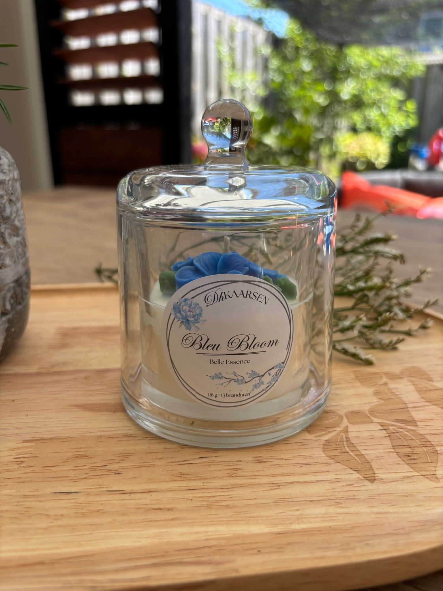 Twee glazen potjes op een houten dienblad, een met een deksel en een met een blauw bloemmotief, in het zonlicht.