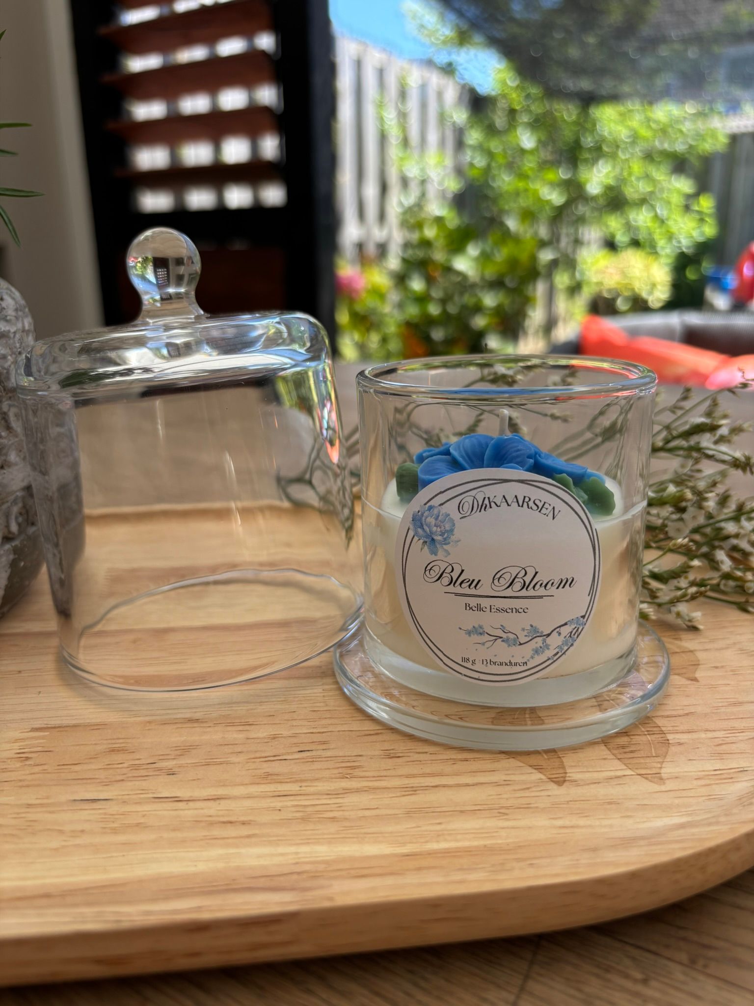 Twee glazen potjes op een houten dienblad, een met een deksel en een met een blauw bloemmotief, in het zonlicht.