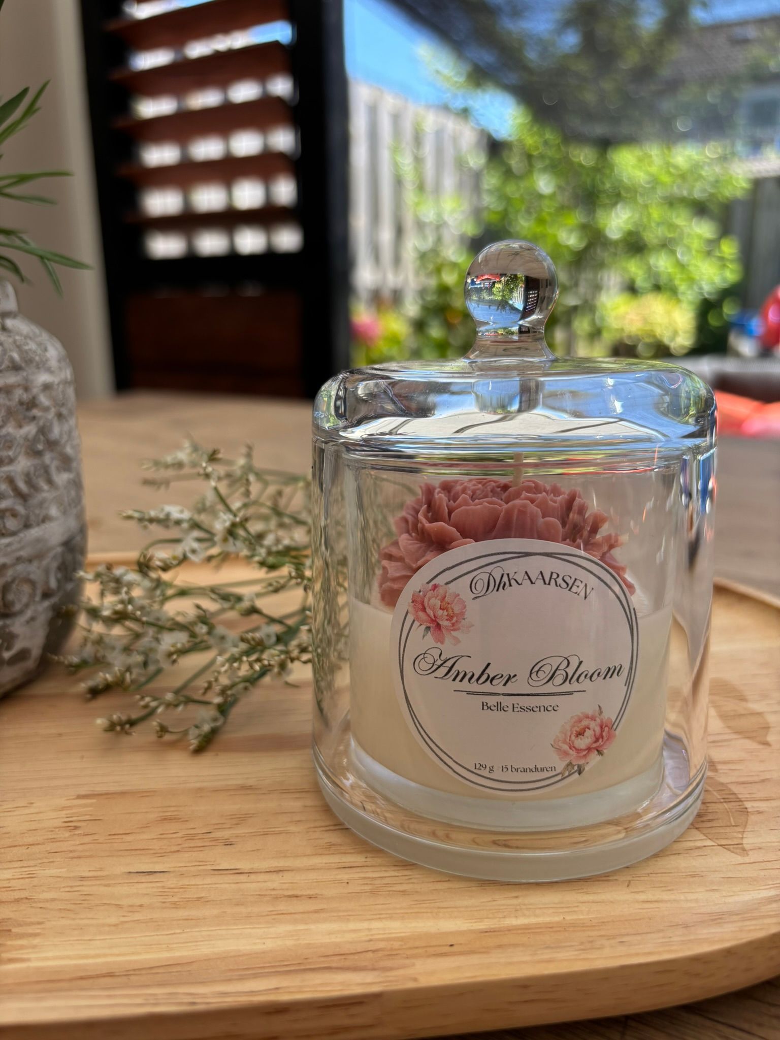 Glazen potjes op een houten dienblad, waaronder een met roze en witte snoepjes, in een lichte binnenomgeving.