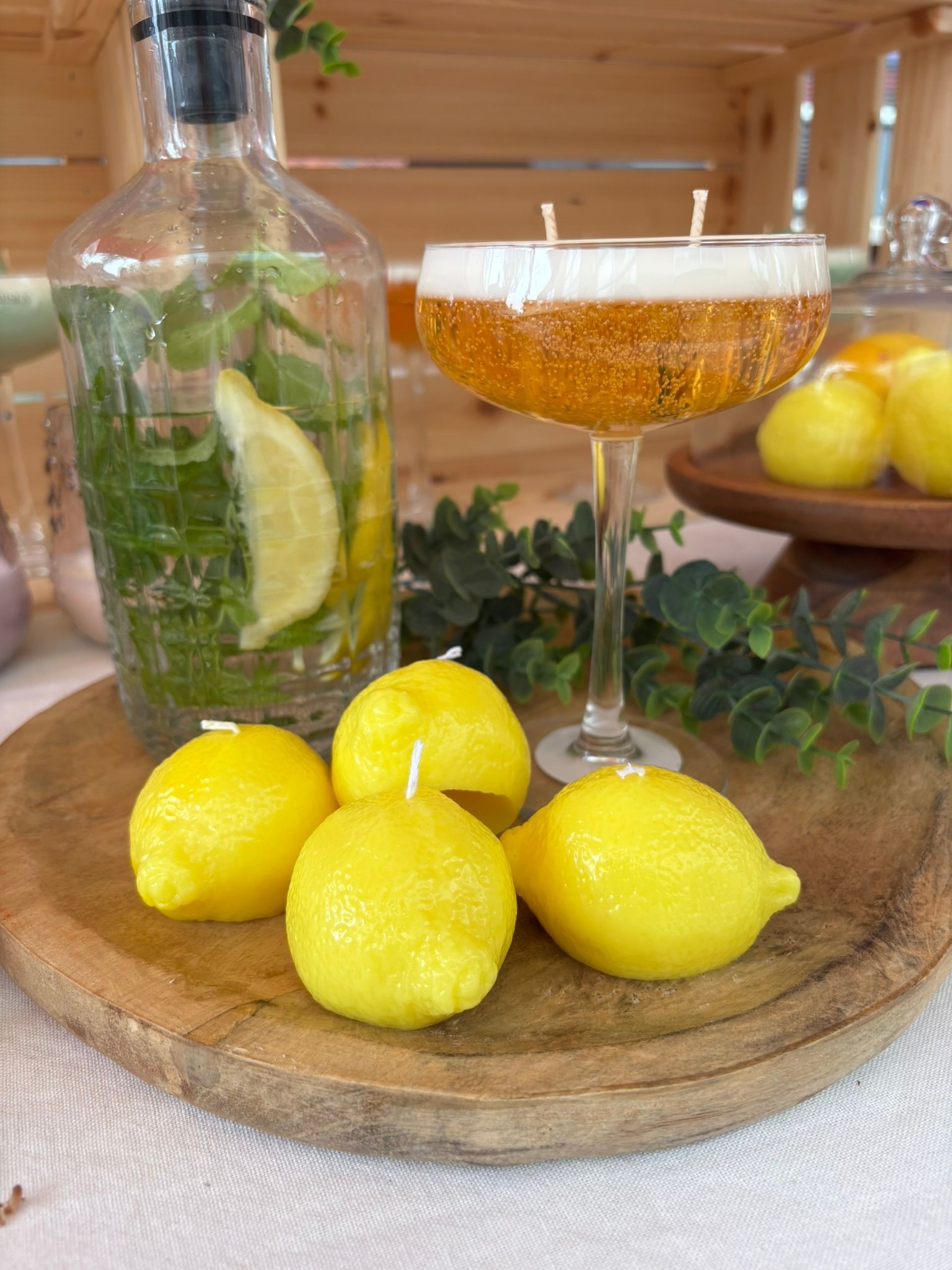 Citroenen op een houten plank naast een glas citrusdrank en een fles met citroenschijfjes en kruiden.