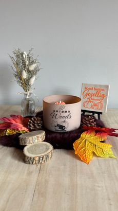 Tafeldecoratie met herfstthema, bestaande uit een kaars, gedroogde bloemen, pompoenen en kleurrijke bladeren op een houten ondergrond.